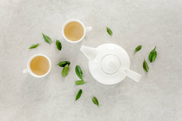 istock Herbal tea with two white tea cups and teapot, with green tea leaves. Flat lay, top view. Tea concept 1276840763