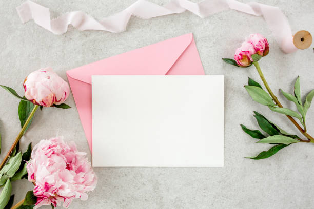 istock Mockup invitation, blank paper greeting card, pink envelope and peonies on gray stone table. Flower background. Flat lay, top view 1276841070