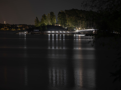 Espoo / Finland - September 26, 2020: A beautiful night skyline of a public leisure island with illuminated walking path and a bridge with calm waters.