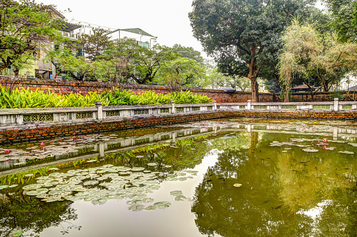 Hanoi, Vietnam - December 31, 2019: The koi fish pond at the Temple of Literature and the Imperial Academy in Hanoi Vietnam, filled with lily pads and surrounded by lush gardens and trees.