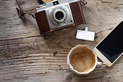 Vintage photo camera. coffee cup and phone on a wooden table at home, flat lay