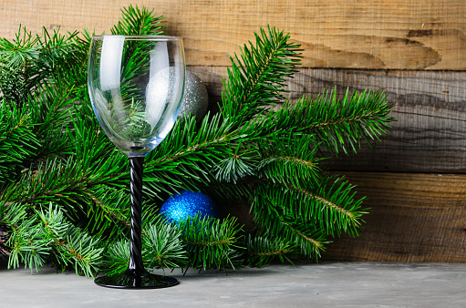 Fir branches with green needles, Christmas balls and one wine glass on a wooden background. Selective focus.