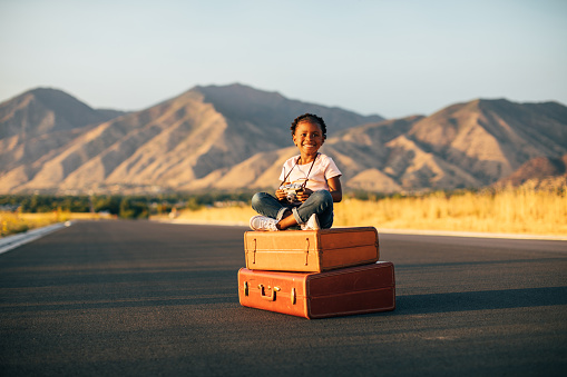 A young girl with a camera has packed her suitcases and is ready to take a vacation even if it is imaginary. She is ready to take pictures at the destination of her dreams. Image taken in Utah, USA.