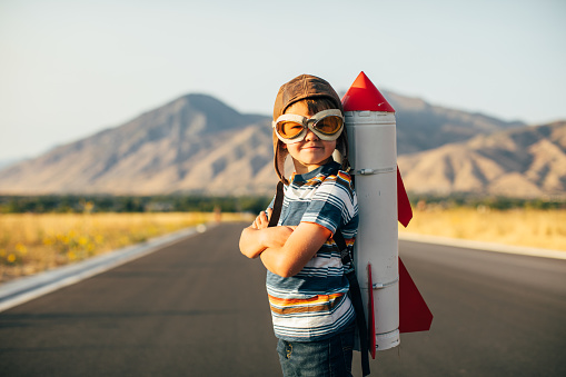 A young boy wearing flying goggles has a rocket strapped to his back as he is ready to fly to new imaginary places. Image taken in Utah, USA.