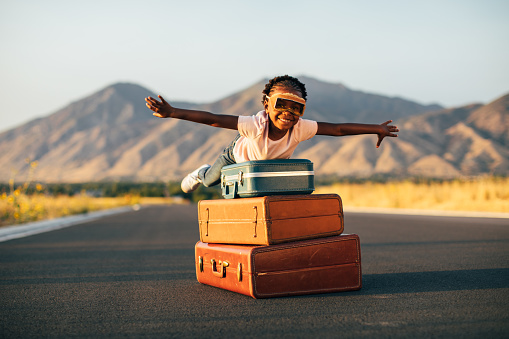 A young girl wearing flying goggles and has packed her suitcases and is ready to take a vacation even if it is imaginary. She is ready to fly away with arms outstretched to the destination of her dreams. Image taken in Utah, USA.