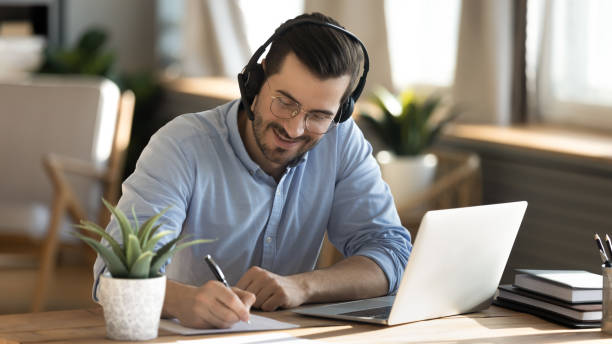 uśmiechnięty kaukaski mężczyzna w słuchawkach studiuje na laptopie - watch watching businessman young adult zdjęcia i obrazy z banku zdjęć