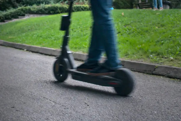 Photo of Riding eco friendly electric scooter at a green park close up on feet