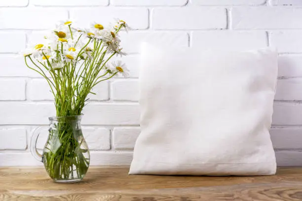 Square cotton pillow mockup with daisy wildflowers in glass pitcher. Rustic linen pillowcase mock up for design presentation