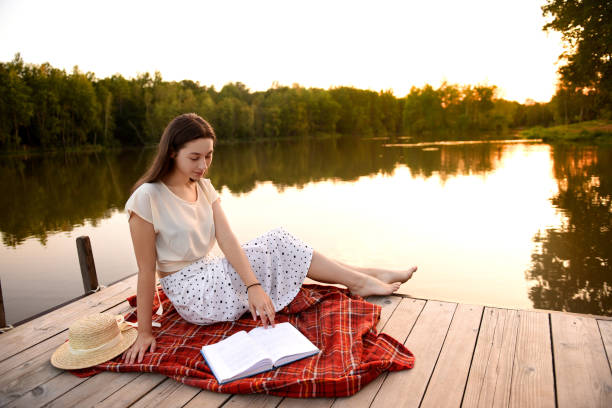 istock Girl on wooden pier. Reads a book. Distance Learning. Quarantine. 1276898953
