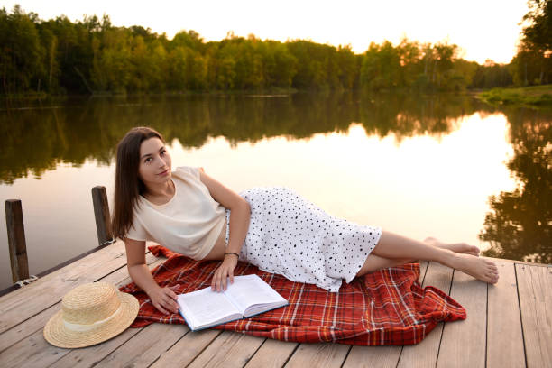 istock Girl on wooden pier. Reads a book. Distance Learning. Quarantine. 1276898974