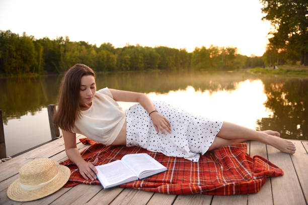 istock Girl on wooden pier. Reads a book. Distance Learning. Quarantine. 1276899576