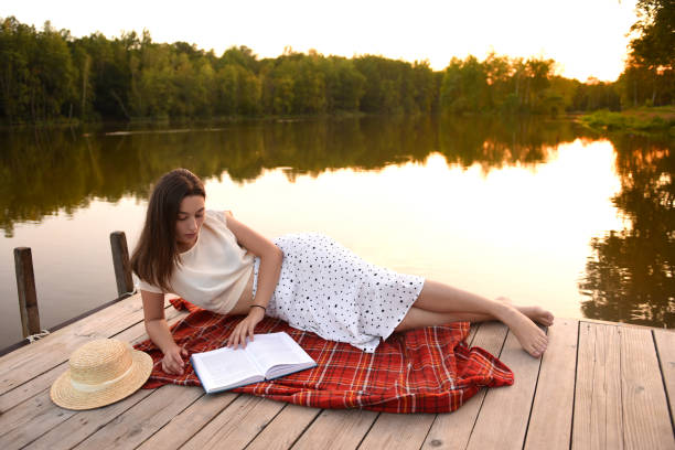 istock Girl on wooden pier. Reads a book. Distance Learning. Quarantine. 1276899595