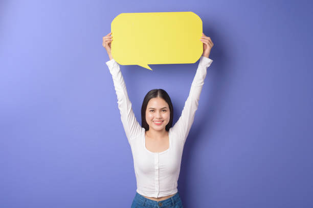 istock Young woman is holding yellow empty speech on purple background 1276902416
