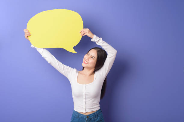 istock Young woman is holding yellow empty speech on purple background 1276902482