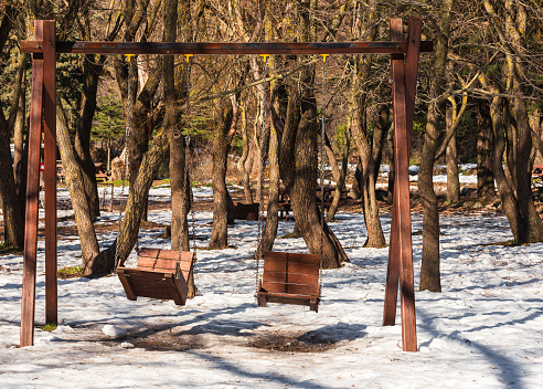 Empty wooden swings in the forest under the snow.