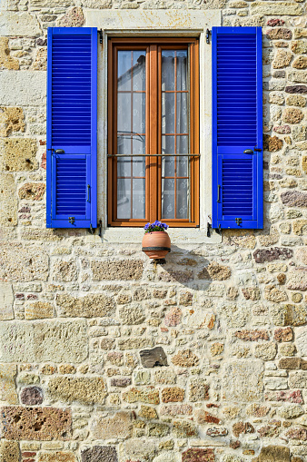 A remarkable window with blue shutters of the stone-walled house.