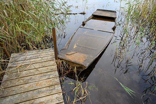 old wooden boat filled with water at jetty in swedish lake
