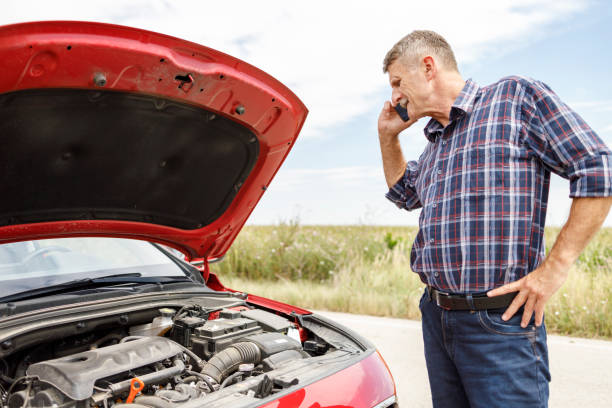 istock Man talking on phone and observing open hood on his  broken car 1276909356