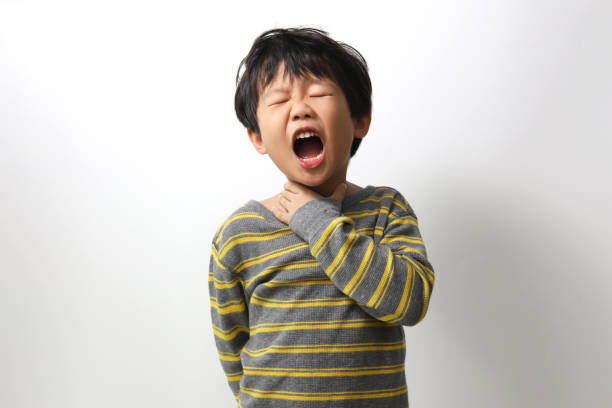 Little Asian boy holding his neck in pain, Sore Throat. stock photo