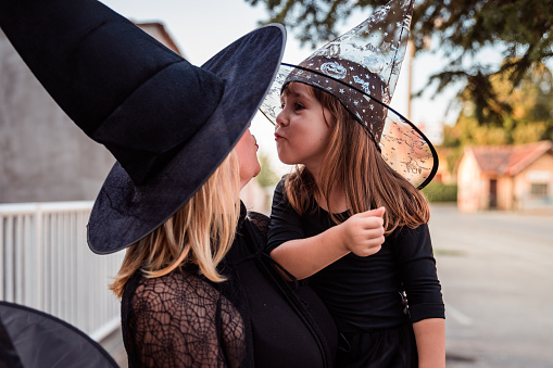 Happy child being held by her mother, both wearing witch Halloween costumes