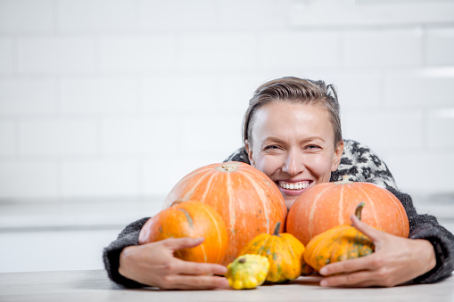 Beautiful woman in sweater with orange pumpkins in white kitchen