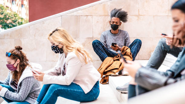 istock Urban millennial people using smart phones with face mask on Covid second wave - Serious guy watching news on mobile smartphone - College students sitting at university break - Bright contrast filter 1276925636