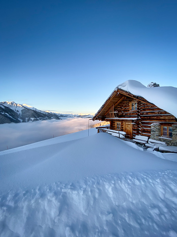 Snow covered mountain hut old farmhouse in the ski region of Saalbach Hinterglemm in the Austrian alps at sunrise against blue sky