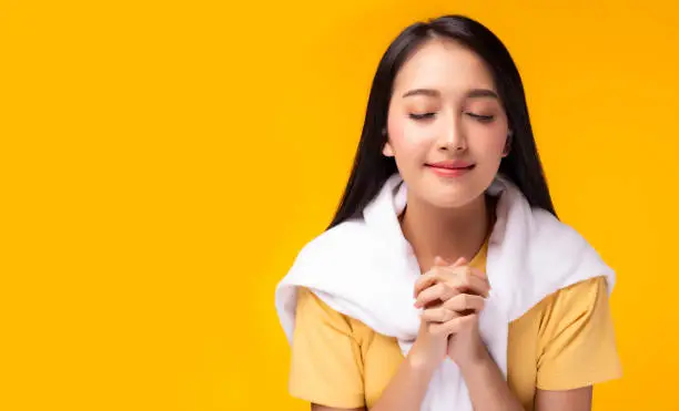 Photo of Dedicated Christian young lady praying to God. Woman praying with hands together on yellow background. Attractive girl thank you for god blessing to wishing have a better life. She believe in goodness