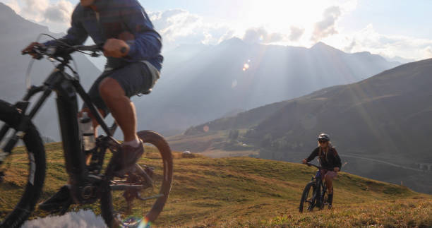 Mountain e-bikers rides up alpine meadow Sun rises over Swiss Alps in distance grindelwald photos stock pictures, royalty-free photos & images