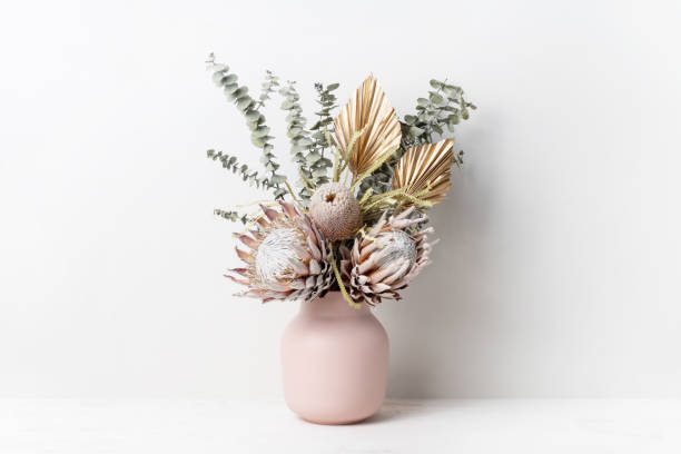Bohemian dried flower arrangement in a stylish pink vase. Beautiful dried flower arrangement in a stylish pink vase. In the flower bunch is pink King Proteas, Banksia, Eucalyptus leaves and golden Palm fronds, photographed on a white background. vase stock pictures, royalty-free photos & images
