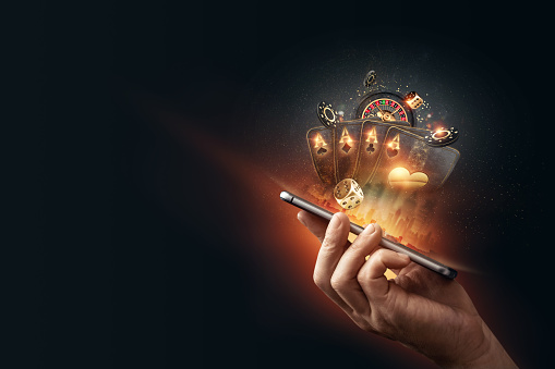 Creative background, online casino, in a man's hand a smartphone with playing cards, roulette and chips, black-gold background. Internet gambling concept. Copy space.