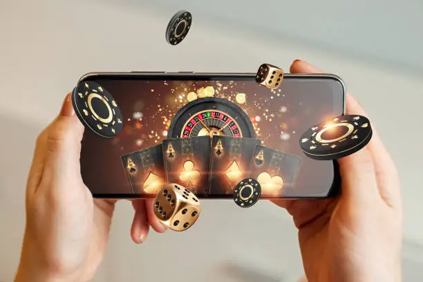 Photo of Creative background, online casino, in a man's hand a smartphone with playing cards, roulette and chips, black-gold background. Internet gambling concept. Copy space