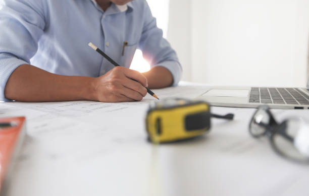 istock Young engineers or architect holding pen and drawing plan on blueprint in working site. 1276940602