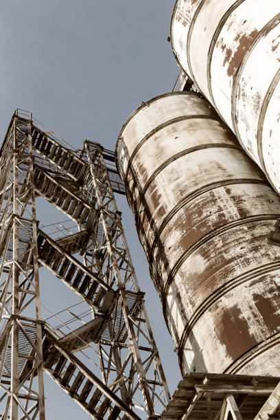 Old, abandoned concrete plant with iron rusty tanks and metal structures. The crisis, the fall of the economy, stop production capacity led to the collapse. Global catastrophe. Old photo effect