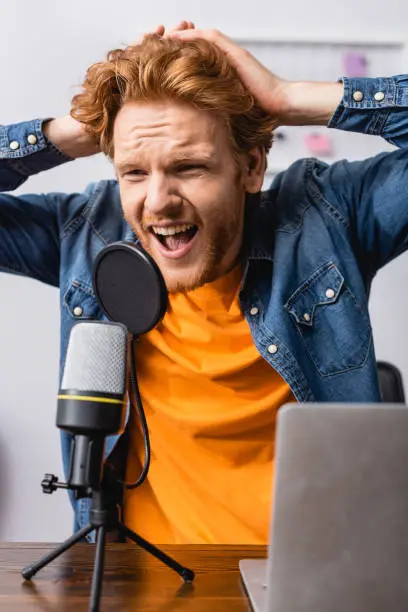 angry announcer touching head while screaming in microphone at workplace