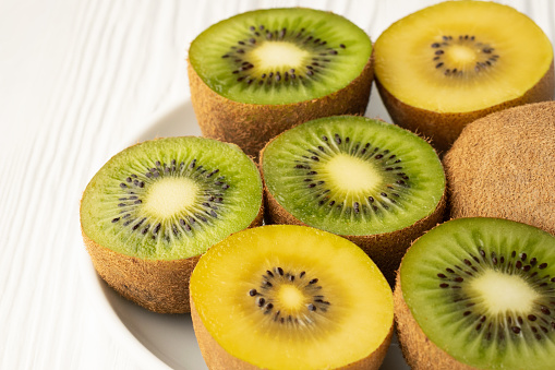 Close up slices of green and yellow golden kiwi in a white plate on the table.