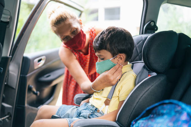 istock Boy wearing protective face mask sitting in the car for his first day back to school while being secured in his car seat by his mother, during COVID-19 1276946149