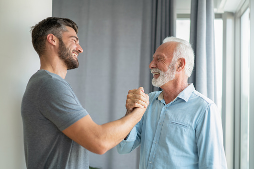 Proud senior man giving high five to his dear son in the living room.