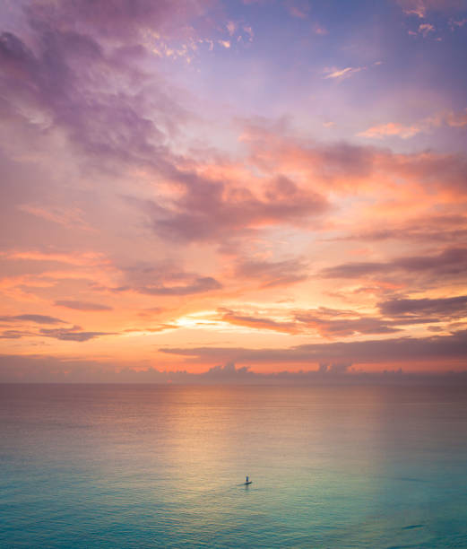 A single stand up paddle boarder AKA SUP rider is going for an early evening cruise on the calm Okinawa waters by the light of a beautiful sunset. Yomitan, Okinawa.