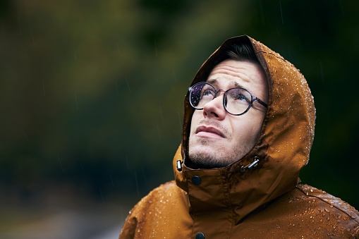 Heavy rain during autumn day. Portrait of young man in waterproof jacket.