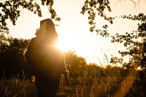 Silhouette of a woman wearing a hat and with a backpack at sunset. Autumn park, copy space.