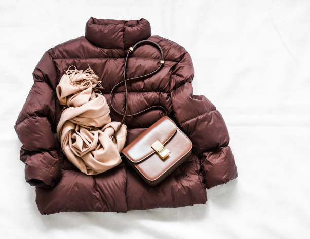 istock Women's brown down jacket, cashmere scarf, leather shoulder bag on a light background, top view. Autumn, winter women's clothing fashion concept 1276967171