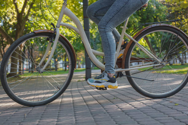 dziewczyna w dżinsach i trampkach jeździ beżowym rowerem w parku wśród zielonych drzew i trawnika - shoe leaving women summer zdjęcia i obrazy z banku zdjęć