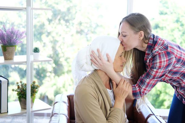 sorridente giovane figlia caucasica si bacia sulla fronte la sua anziana madre in velo bianco dopo la chemioterapia perché soffre di cancro o paziente con leucemia. - cancer chemotherapy drug baby family foto e immagini stock