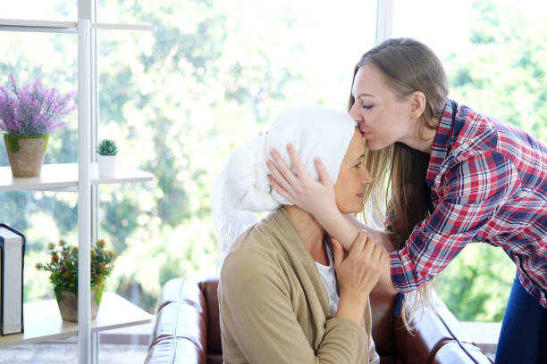 笑顔の白人の若い娘は、彼女が癌や白血病患者に苦しんでいるので、化学療法の後、白いヘッドスカーフで彼女の高齢の母親の額にキスをしています。 - senior adult family cheerful couple ストックフォトと画像