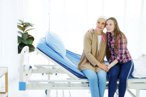 sorridente madre anziana caucasica in velo bianco è seduta con la giovane figlia a letto insieme in ospedale dopo la chemioterapia perché soffre di cancro o paziente con leucemia. - cancer chemotherapy drug baby family foto e immagini stock