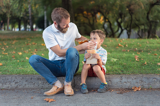 Father and little son spending time together and eating burgers in the park