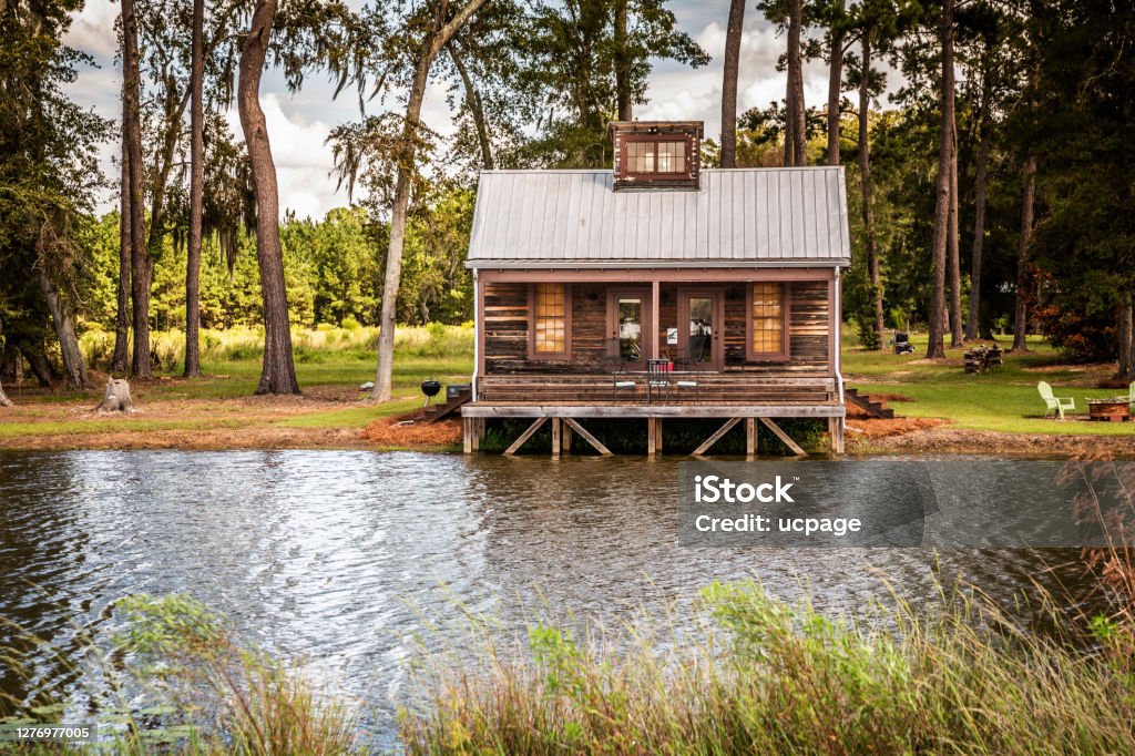 Scenic view of the exterior of a rural rustic wooden camp house used for fishing and hunting. The house is located on a large pond Log Cabin Stock Photo