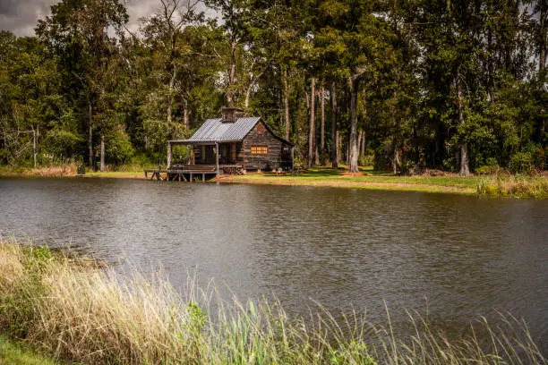 Photo of Expanse view of the exterior of a rural rustic wooden camp house used for fishing and hunting. The house is located on a large pond