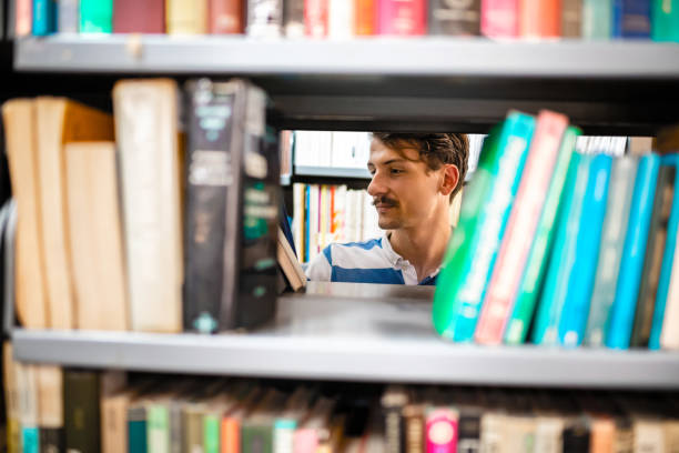 Focused and determined male University student looking for a right literature between bookshelves at the University library